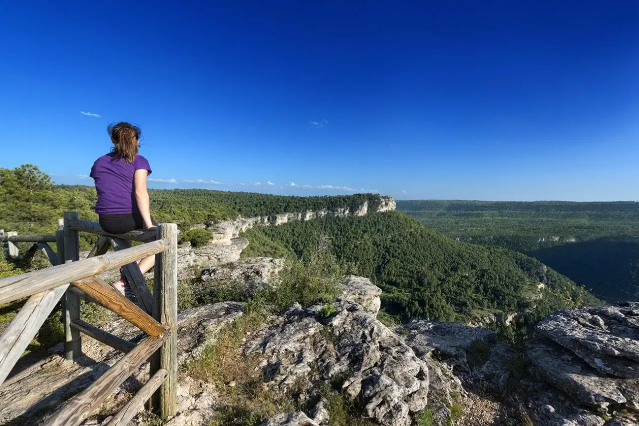 Mujer contempla un paisaje de ca&ntilde;ones y bosques verdes en Castilla-La Mancha, un lugar ideal para recorrer las v&iacute;as pecuarias.
