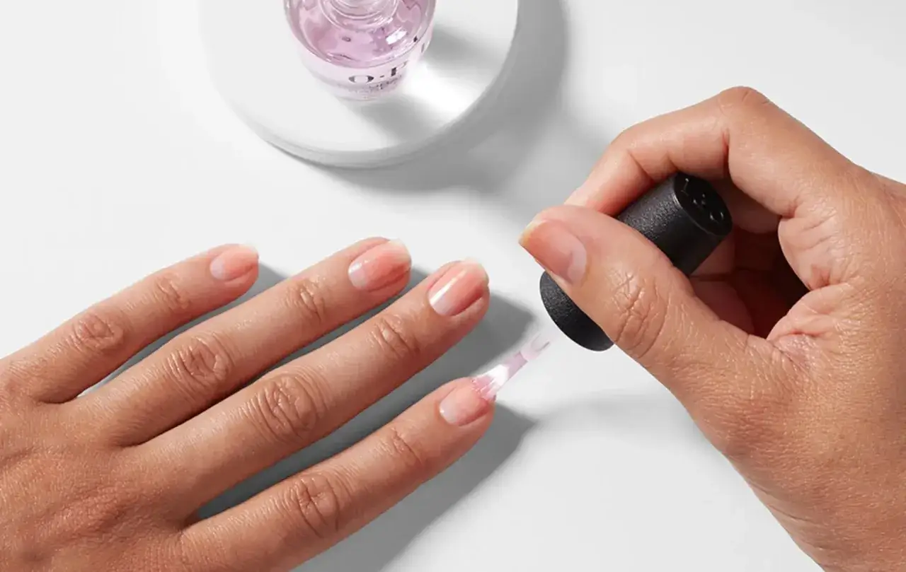 Application d'une base coat sur un ongle naturel. Ce produit prépare l'ongle pour le vernis, assurant une meilleure adhérence et protection.