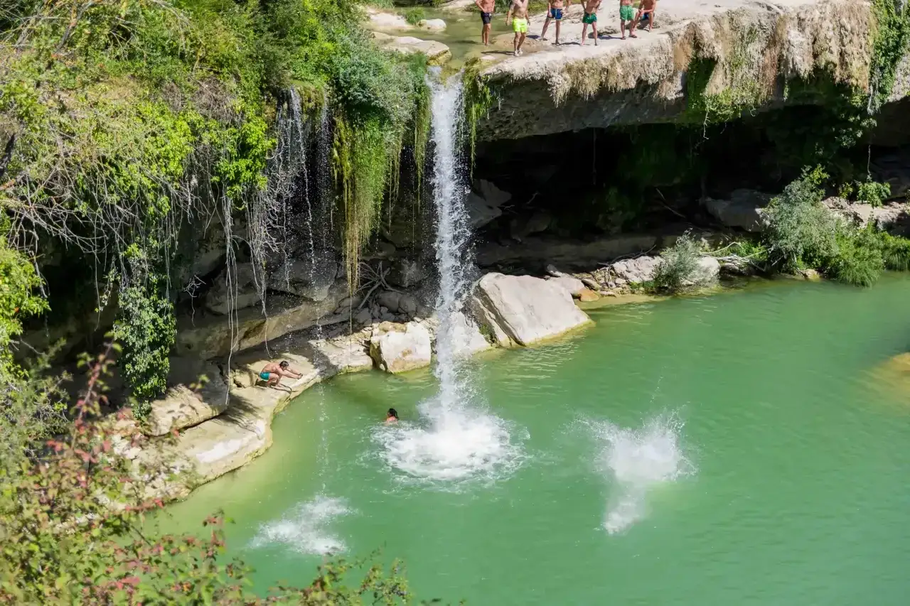 Un grupo de jóvenes disfruta de las cascadas en León, saltando a la poza de agua turquesa.