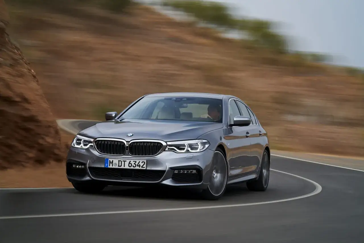 Srebrne BMW M5 G30 pokonuje zakręt na górskiej drodze, ukazując swoją dynamikę.