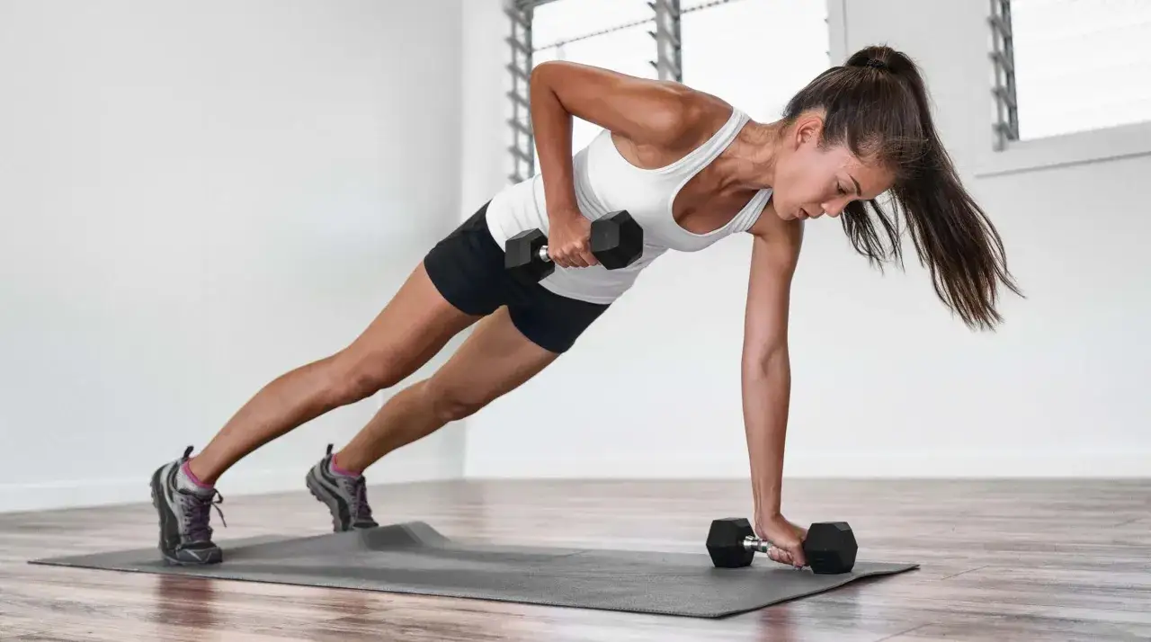 Kobieta wykonuje ćwiczenie z hantlami w pozycji deski, intensywny trening hiit.