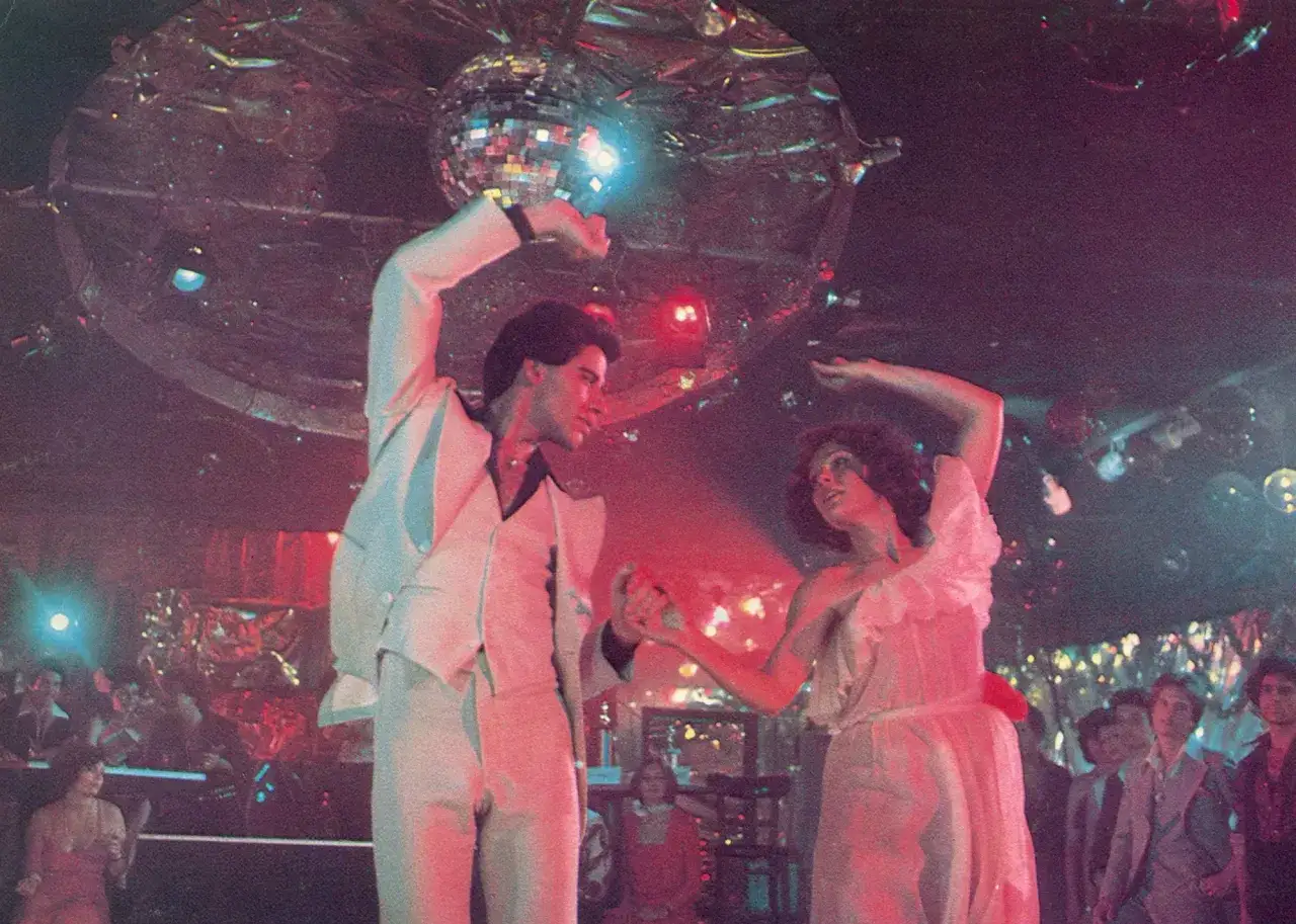 Un couple danse sous une boule disco, l'ambiance est à son apogée, c'est l'année disco.