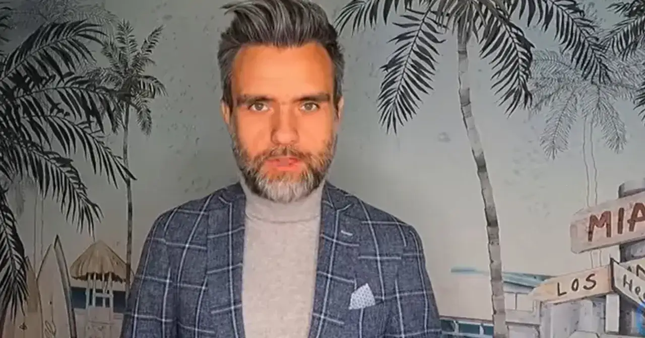 Niedziela, redaktor TVN, w marynarce w kratę i golfie, na tle tropikalnej tapety z palmami i tabliczkami kierunkowymi.