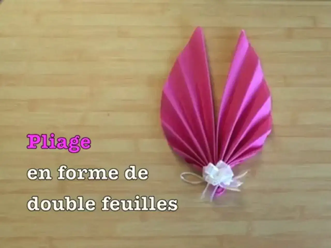 Pliage serviette palmier, une création élégante en forme de double feuilles, décorée d'un nœud blanc.