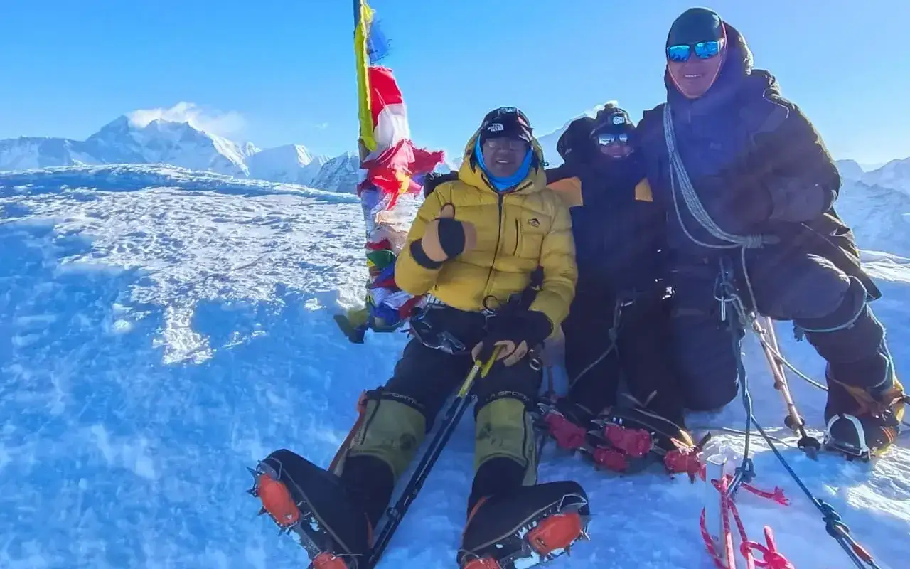 Trzech alpinistów na szczycie Mera Peak, z modlitewnymi flagami i lodowymi rakami.
