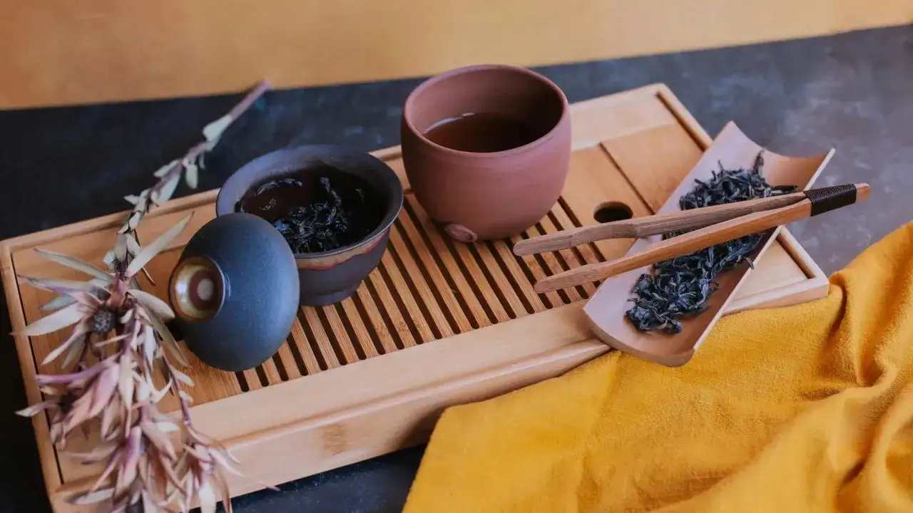 Ceremonia parzenia herbaty oolong: suszone liście, gliniane naczynia i ozdobna gałązka.