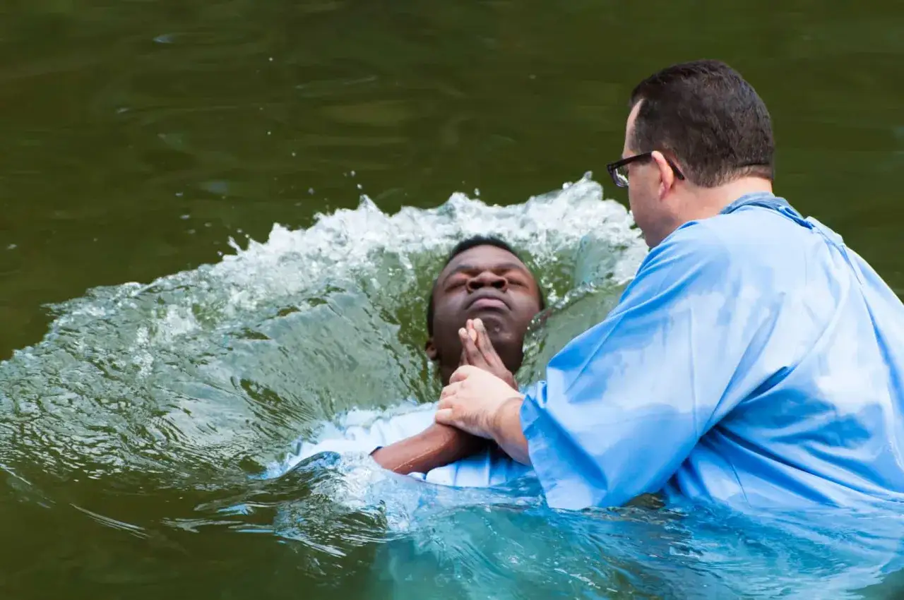 A man is baptized in water by another man, a symbolic act for salvation.