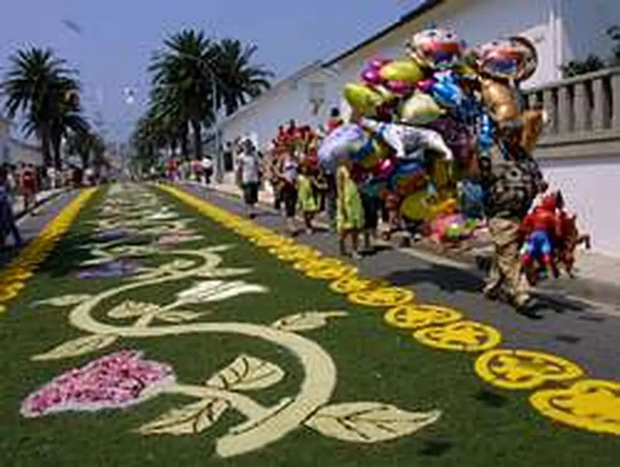 Alfombra floral para las fiestas del Carmen en Foz. Gente pasea por la calle adornada con flores y globos.