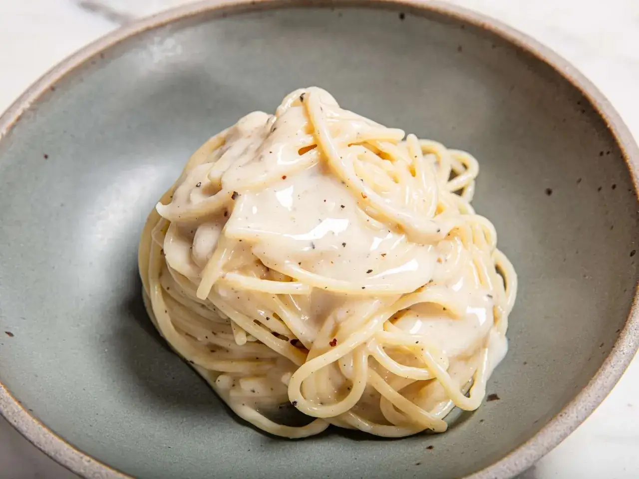 En krämig portion cacio e pepe, spaghetti täckt med en len ost- och pepparsås, serverad i en grå skål.