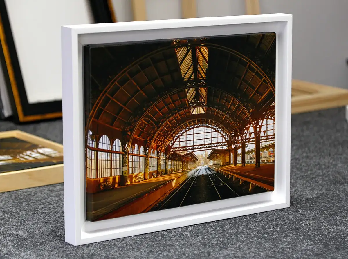 Une gare majestueuse, baign&eacute;e de lumi&egrave;re dor&eacute;e, est mise en valeur par un cadre blanc moderne. L'art de **encadrer une toile** sublime cette sc&egrave;ne architecturale.