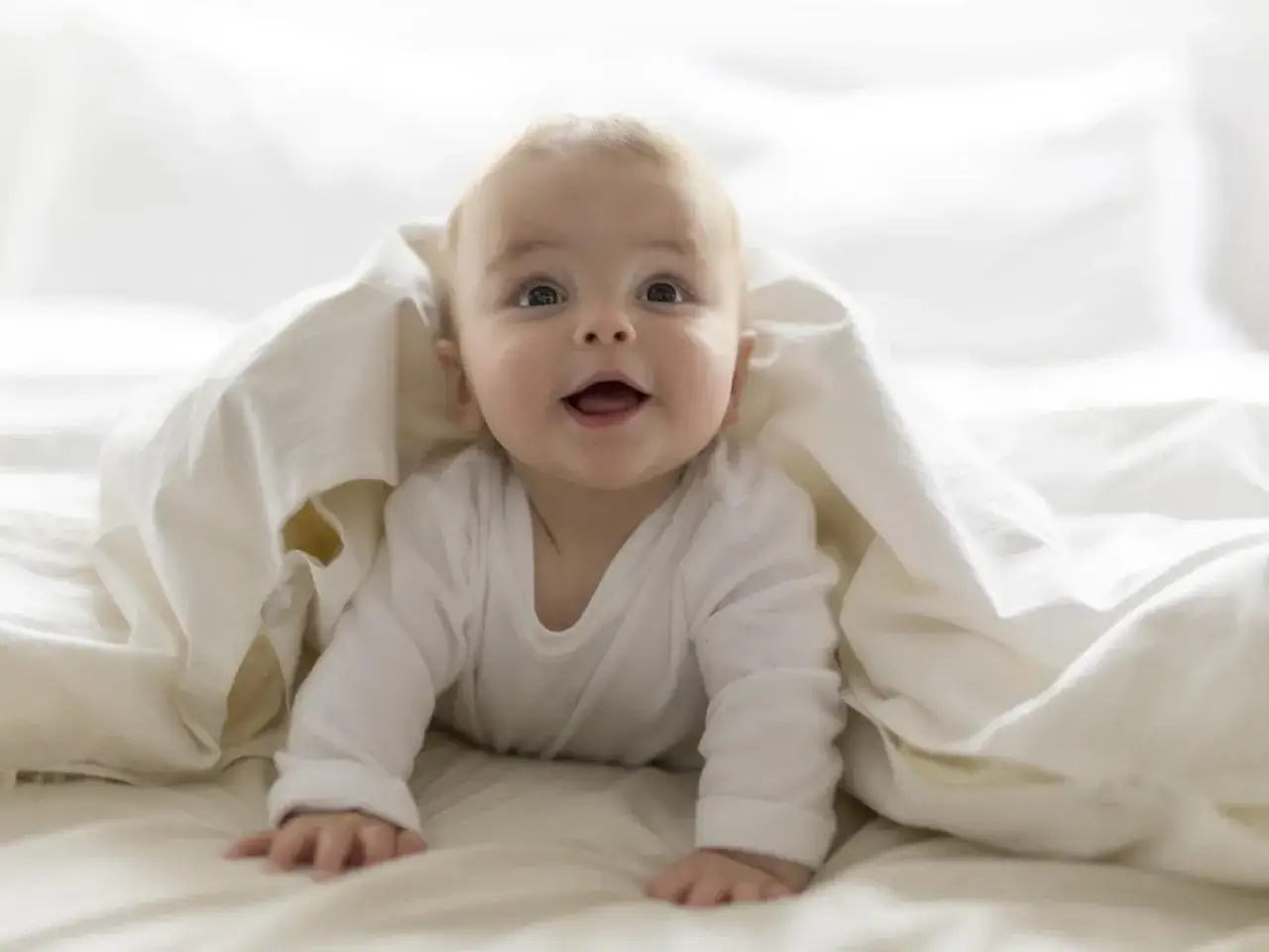 Ein lächelndes Baby versteckt sich unter einer Decke. Vielleicht ein zukünftiger Noah oder ein kleiner David, inspiriert von Jungennamen Bibel.
