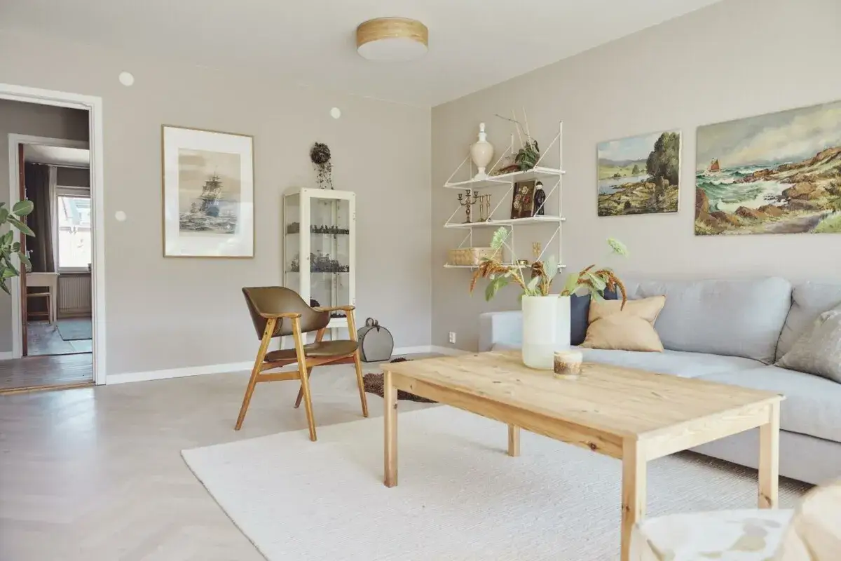 Sal&oacute;n acogedor con sof&aacute; gris, mesa de madera y una **pintura que disimula imperfecciones** en la pared.