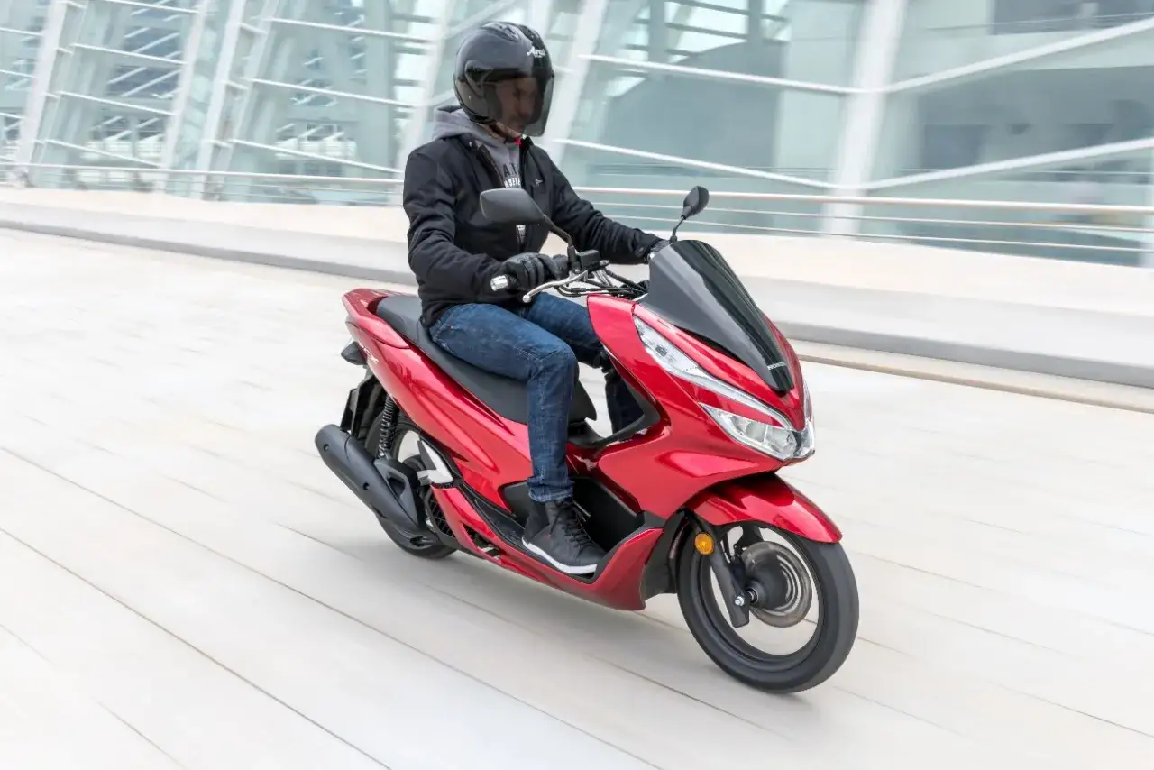 Czerwony skuter Honda PCX 125 w ruchu. Kierowca w kasku i jeansach, testuje możliwości pojazdu, choć wady mogą się ujawnić w trudniejszych warunkach.
