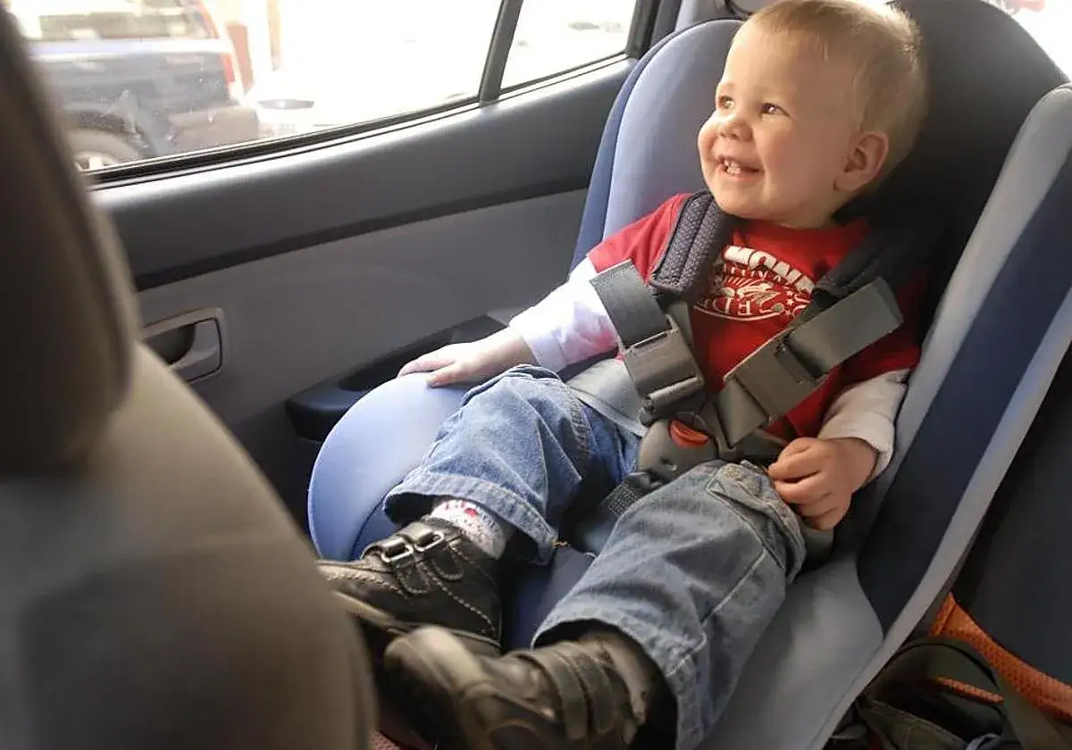 Niño sonriente en silla de auto, con cinturón de seguridad. Cumple con la norma ECE R44/04, asegurando su vigencia y seguridad.