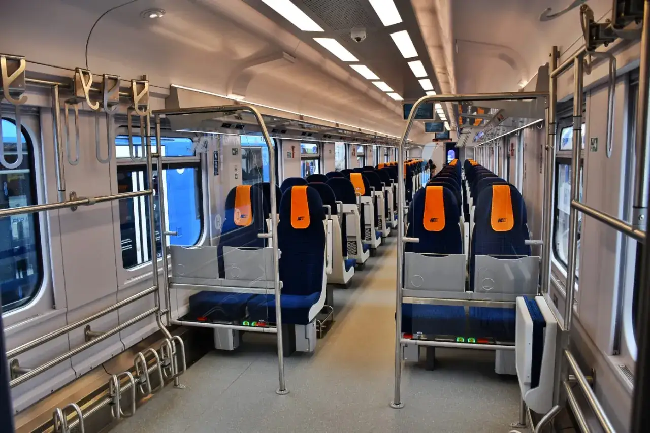 Wnętrze wagonów IC 3806 Malczewski. Ciemnoniebieskie siedzenia z pomarańczowymi zagłówkami ustawione w rzędach.