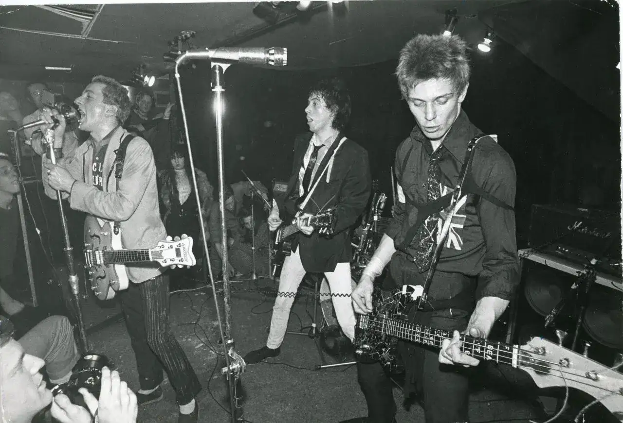 Drei britische Punk-Bands auf der B&uuml;hne, ein S&auml;nger mit Mikrofon, Gitarristen und Bassisten, die ihre Instrumente spielen.