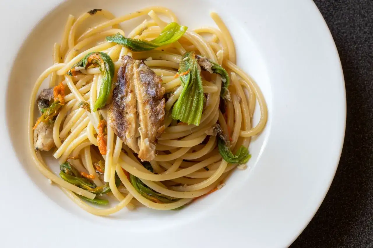 Spaghetti con fiori di zucca e pesce, un piatto estivo che profuma di mare e orto.