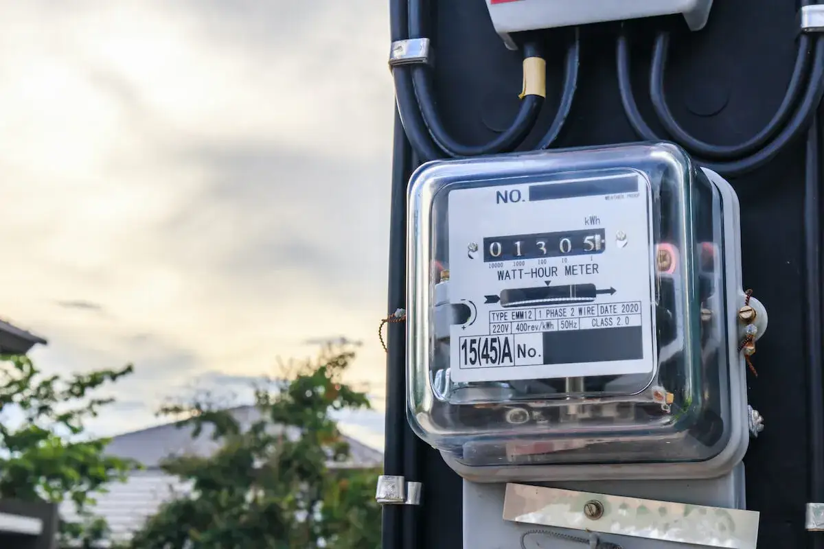 Licznik energii elektrycznej, który może sugerować próby jak oszukać licznik prądu. W tle dom i niebo.
