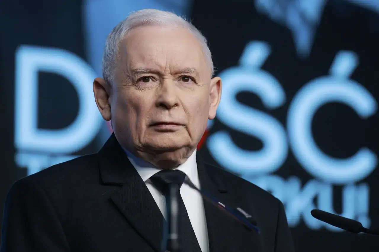 Jarosław Kaczyński, lider partii, w garniturze przed niebieskim tłem z napisem