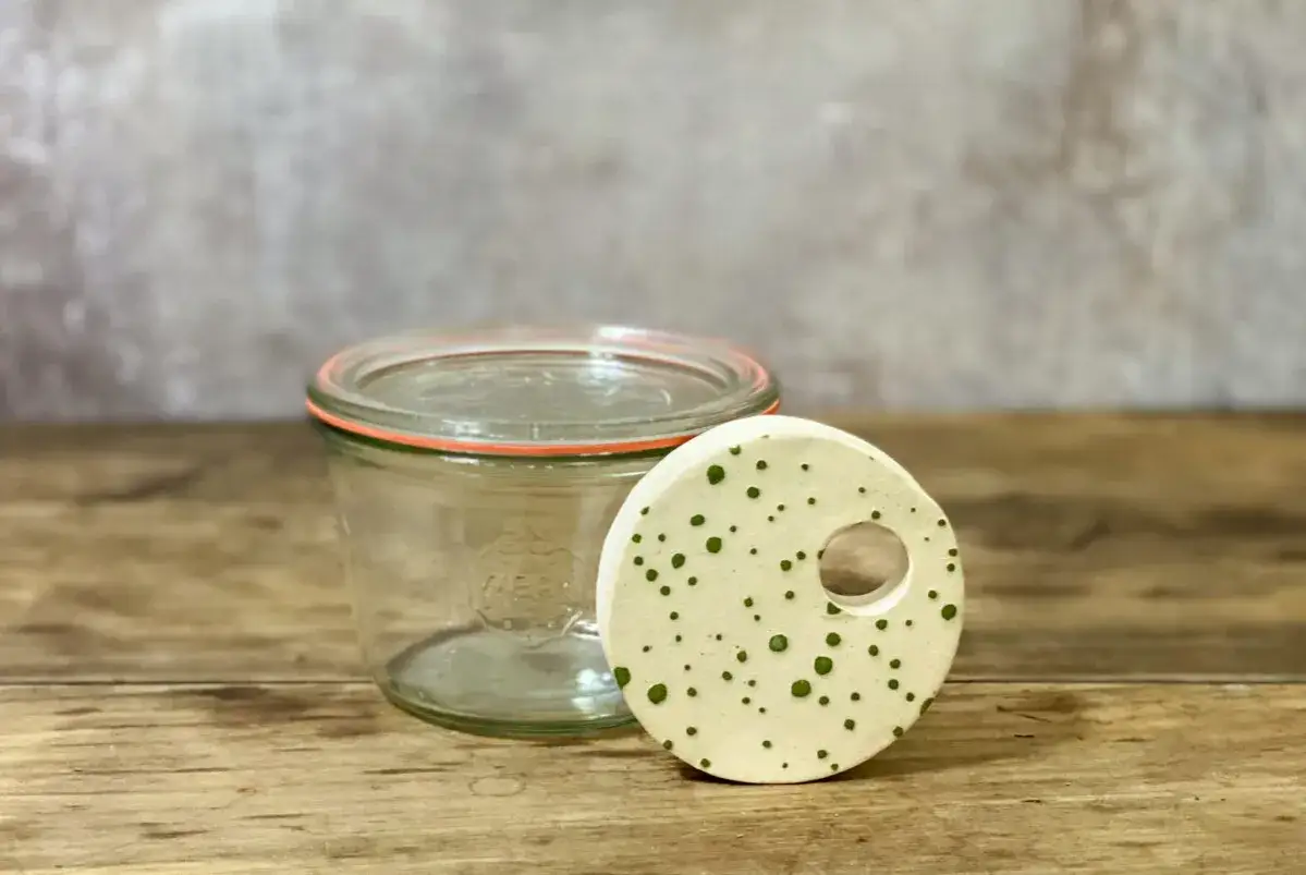 Ein Glas mit Deckel und ein selbstgemachtes Gewicht zum Fermentieren, verziert mit grünen Punkten.