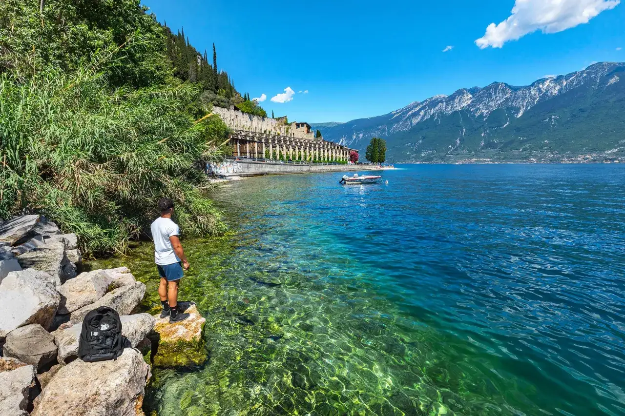 Ragazzo ammira il limpido lago di Garda vicino a Tignale, con montagne sullo sfondo.