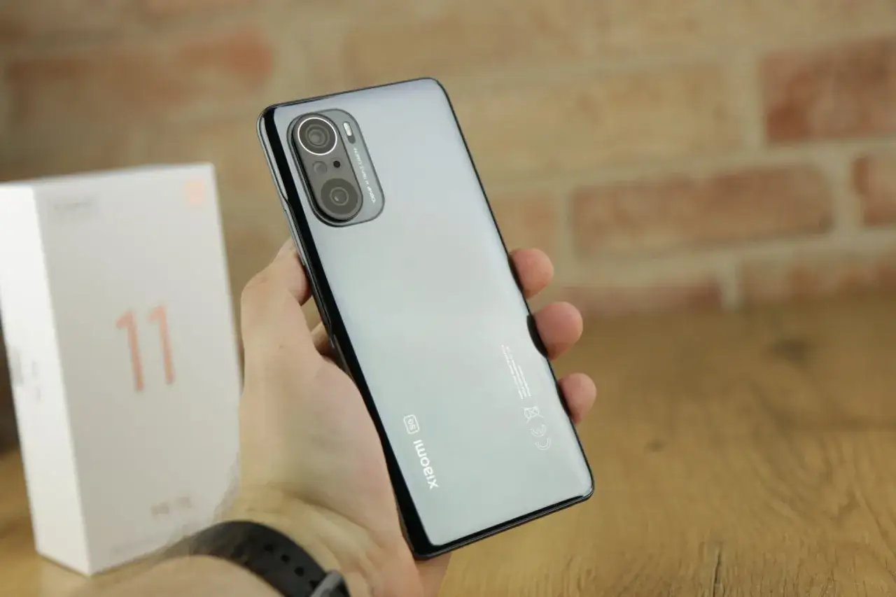 Dłoń trzyma błyszczący telefon Xiaomi 11i z potrójnym aparatem. Obok stoi białe pudełko z cyfrą 11.
