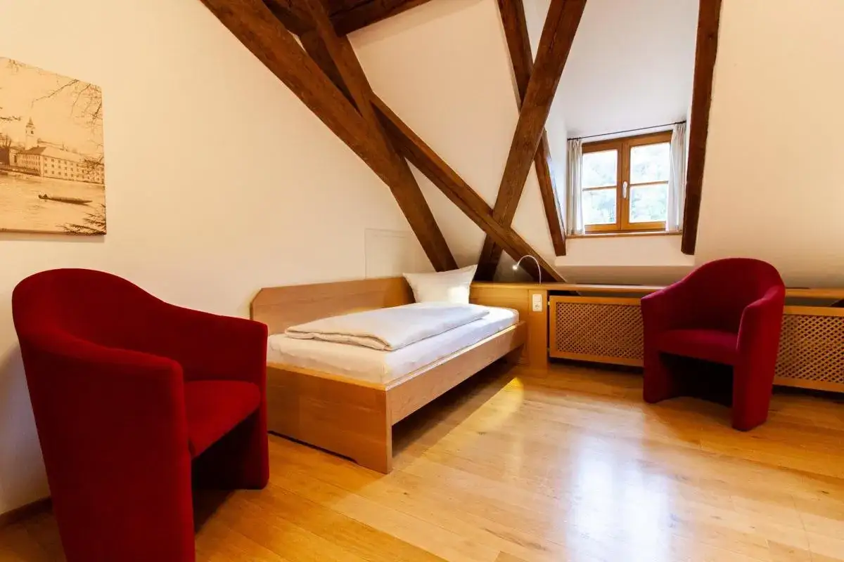 Gemütliches Zimmer mit Holzbalken und zwei roten Sesseln. Perfekt für eine **Auszeit im Kloster**.