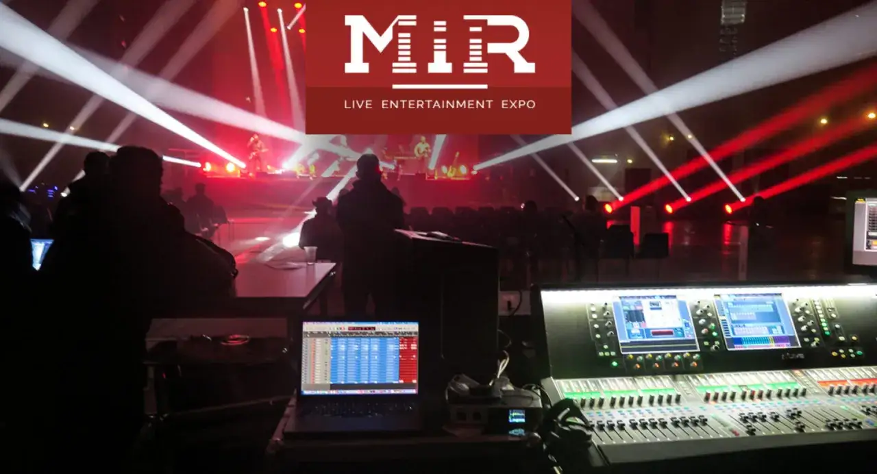 Dietro le quinte di un concerto al MIR Fiera Rimini, con luci stroboscopiche e console audio.