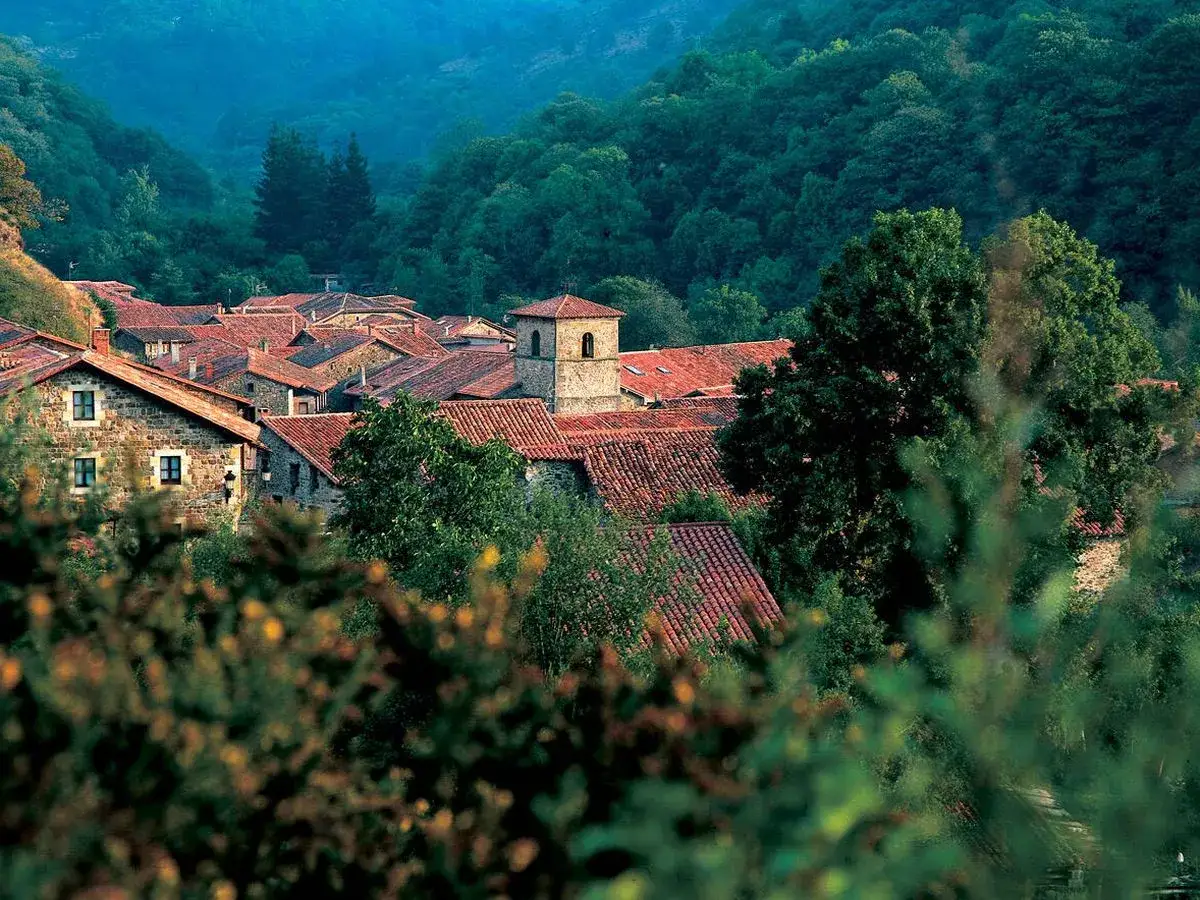 Un pueblo con tejados rojos y un campanario, rodeado de verdes colinas. Un ejemplo de los pueblos bonitos cerca de Li&eacute;rganes.