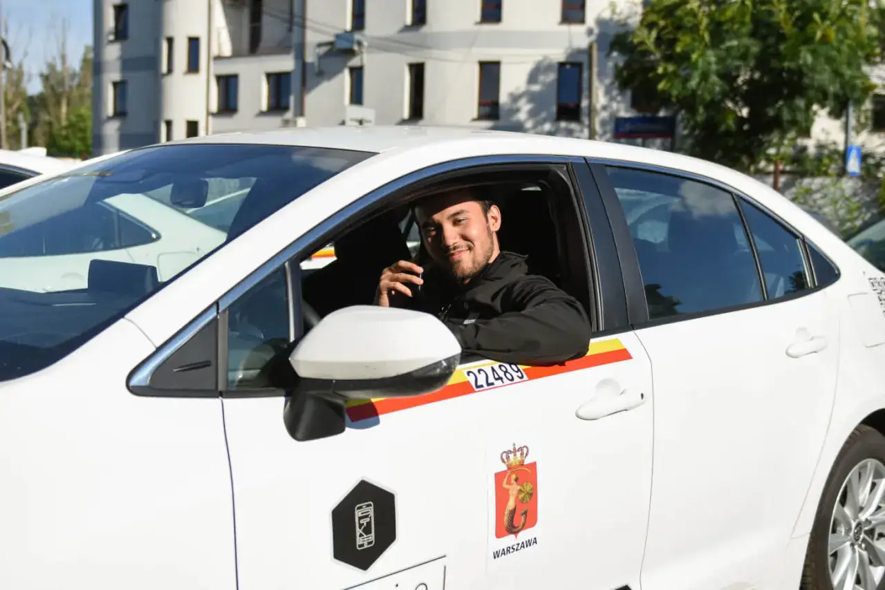 Uśmiechnięty kierowca w białym aucie z logo Warszawy. Chcesz wiedzieć, jak zostać kierowcą Ubera? To może być Tw&oacute;j nowy cel!