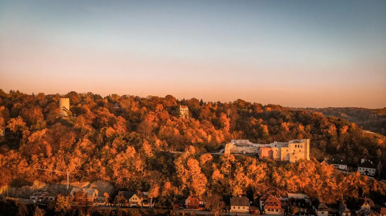 Zabytkowe miasto nad Wisłą w jesiennej szacie. Widać ruiny zamku, wieżę i domy w otoczeniu kolorowych drzew.