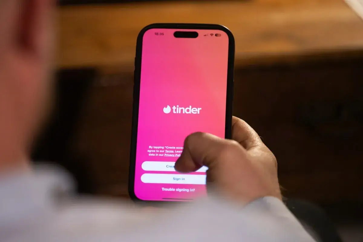Dłoń trzyma smartfon z ekranem logowania Tindera. Czekam na powiadomienia.