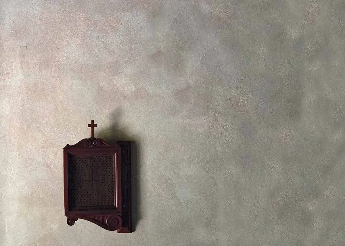 Pittura tamponato grigio con un'antica cornice di legno scuro che racchiude un simbolo religioso.