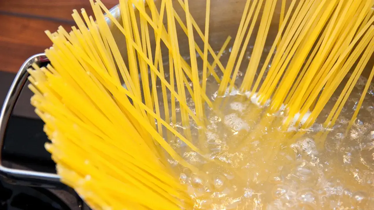 Gelbe Spaghetti kochen in sprudelndem Wasser. Der Topf ist aus Metall und steht auf einer dunklen Oberfl&auml;che.