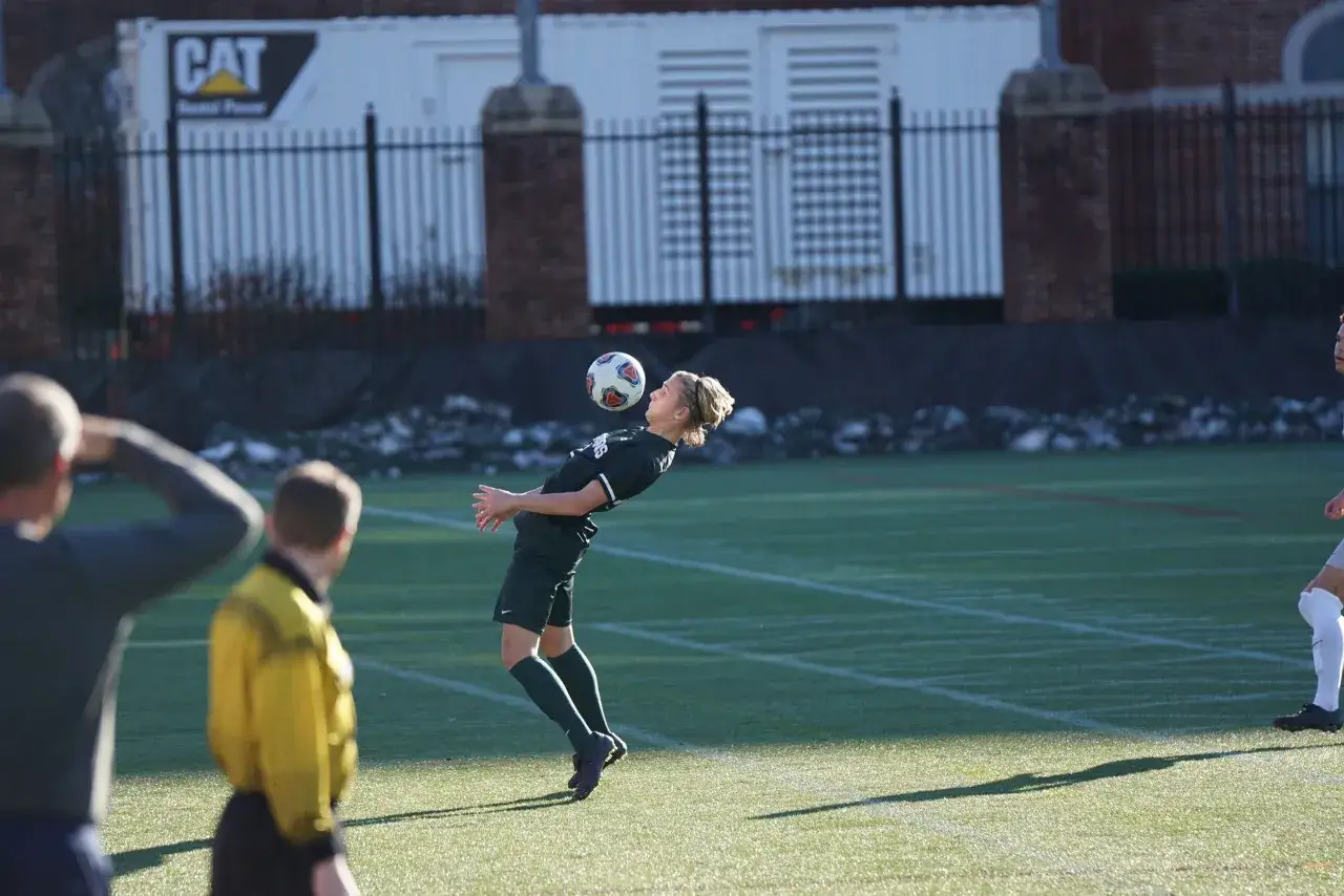 Ein Fu&szlig;baller mit blonden Haaren jongliert den Ball mit dem Kopf. Ein Scout beobachtet das Spiel, um Talente zu entdecken.
