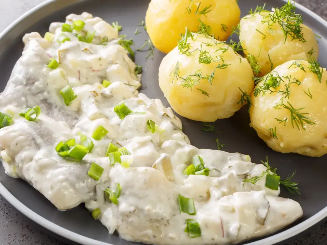 Pyszne śledzie w śmietanie z koperkiem i szczypiorkiem, podane z ziemniakami.