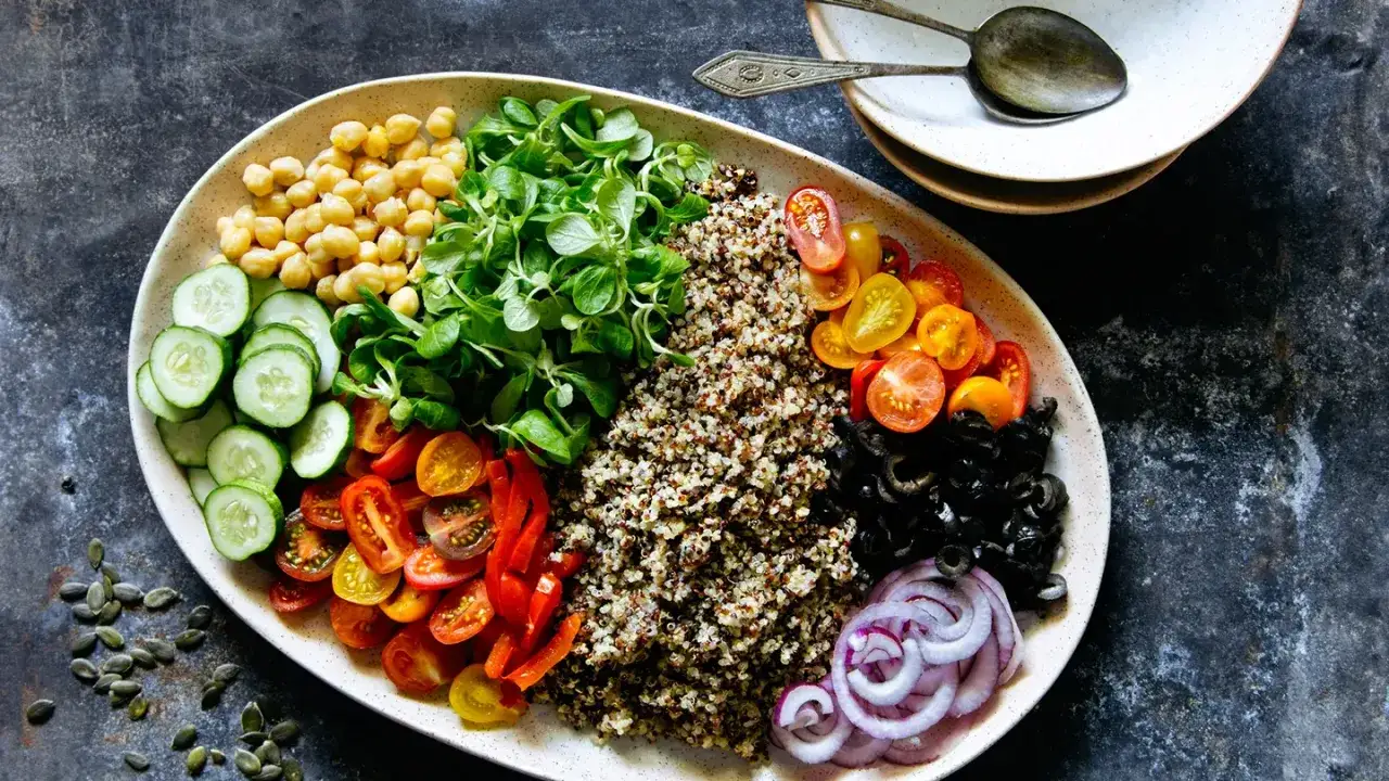 Piatto colorato con ceci, quinoa, pomodorini, olive, cipolla rossa, cetrioli e verdure a foglia verde. Ideale per chi cerca cosa mangiare con glicemia alta.