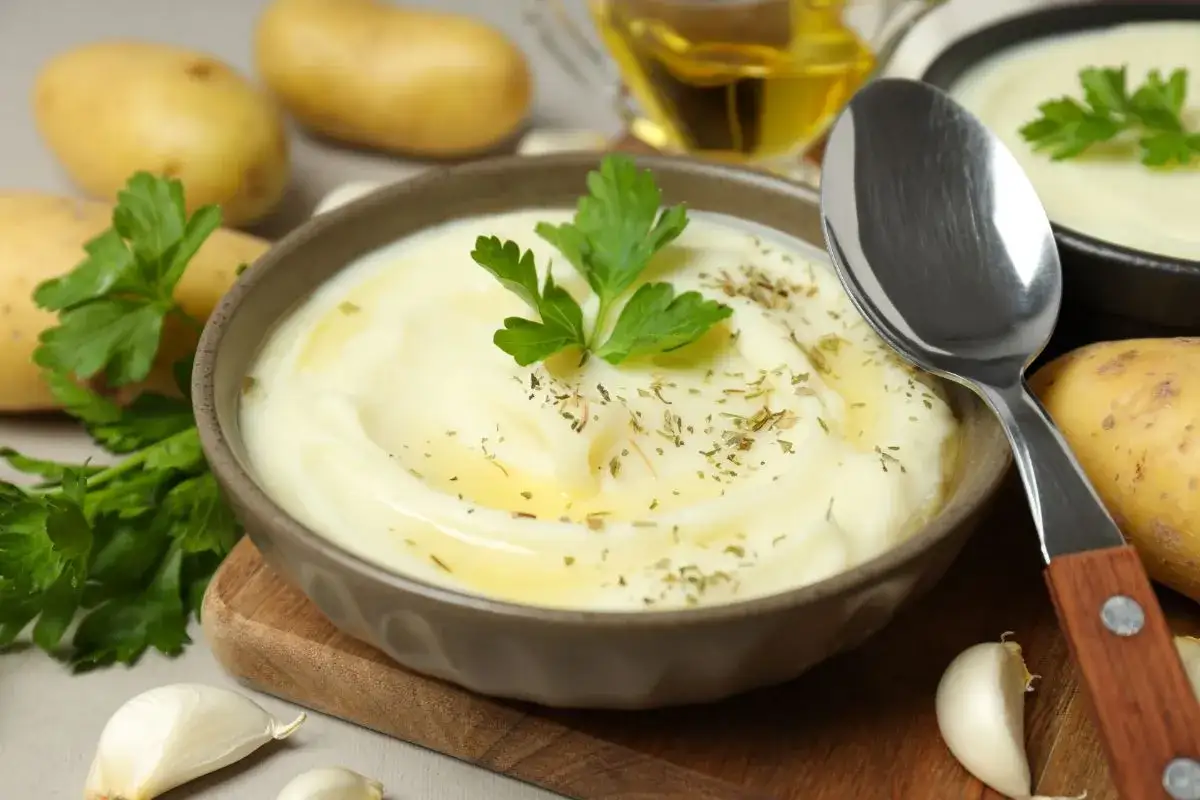 Un bol de purée onctueuse, un écrasé de pomme de terre savoureux, garni de persil frais et d'herbes. Des pommes de terre crues, de l'ail et de l'huile d'olive complètent la scène.