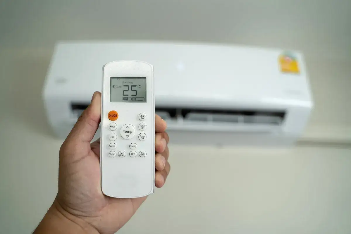 Mano che tiene il telecomando per impostare climatizzatore aria fredda a 25&deg;C.