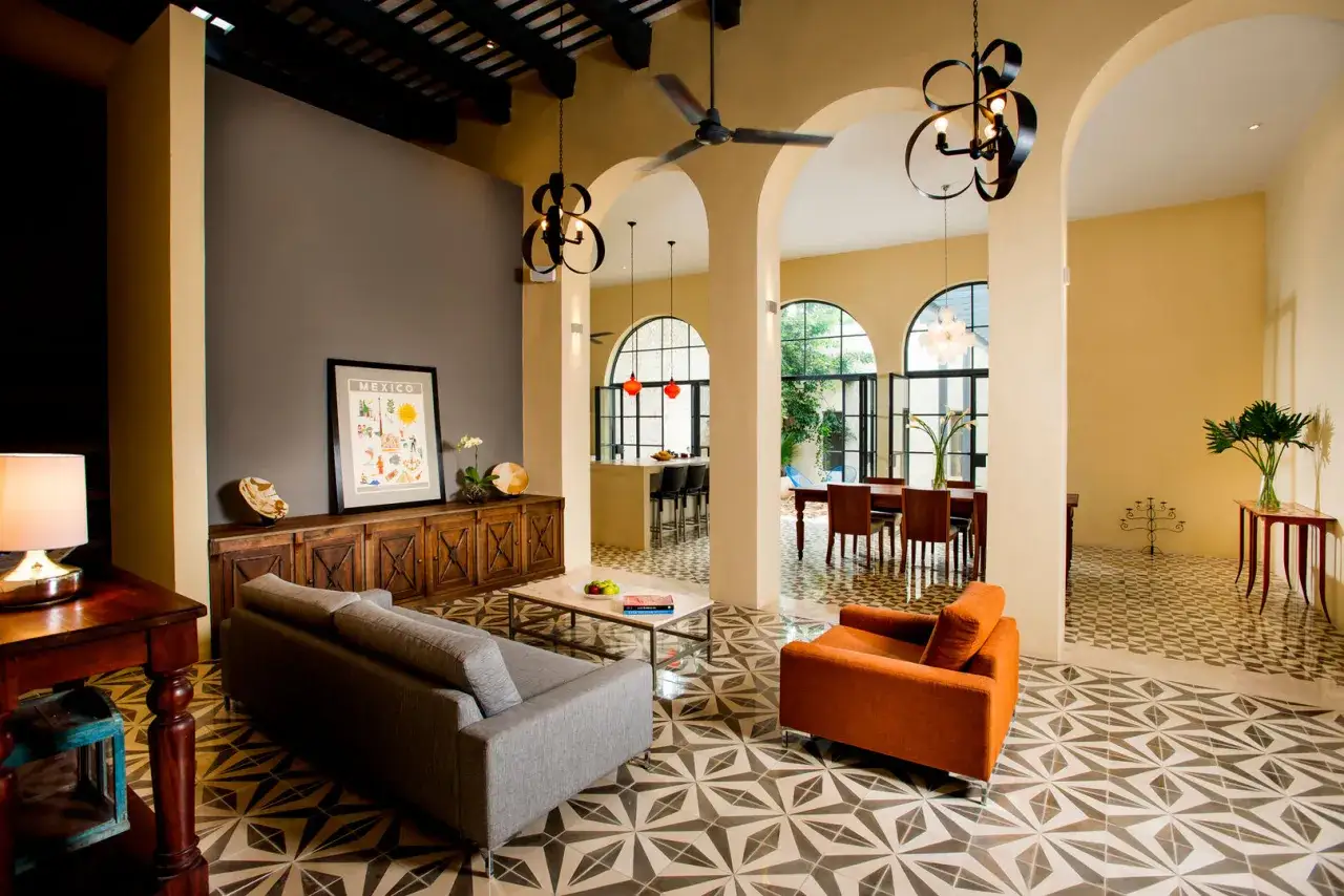 Sofá gris y sillón naranja en un salón con suelo de baldosas geométricas. Las paredes en tonos tierra y ocre crean cálidos colores para salones.