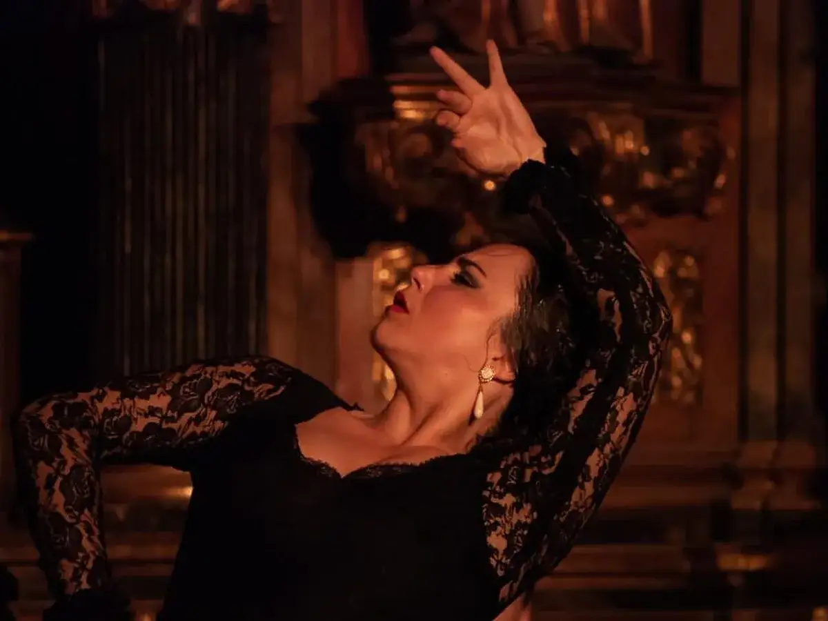 Una bailaora de flamenco eleva sus manos, con encaje negro en sus brazos, en un gesto apasionado.