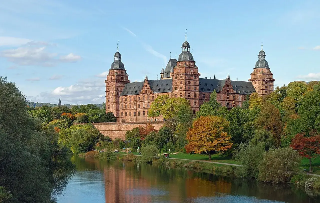 Schloss Johannisberg, ein prächtiges Bauwerk, spiegelt sich im Wasser. Die Herbstfarben der Bäume um das Schloss von Bibra sind leuchtend.