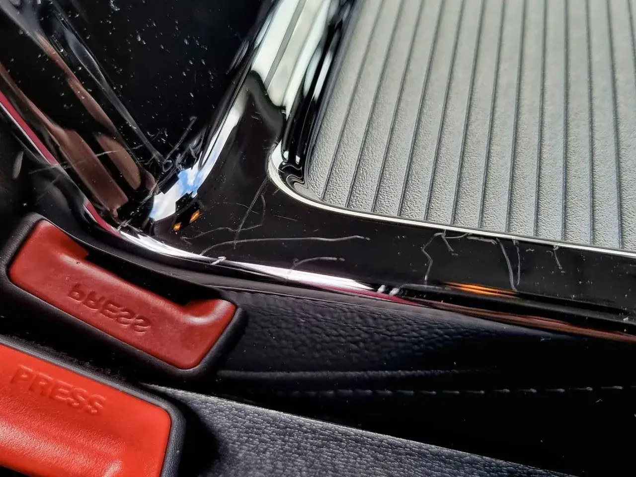Błyszczące piano black z licznymi rysami, widoczne czerwone przyciski