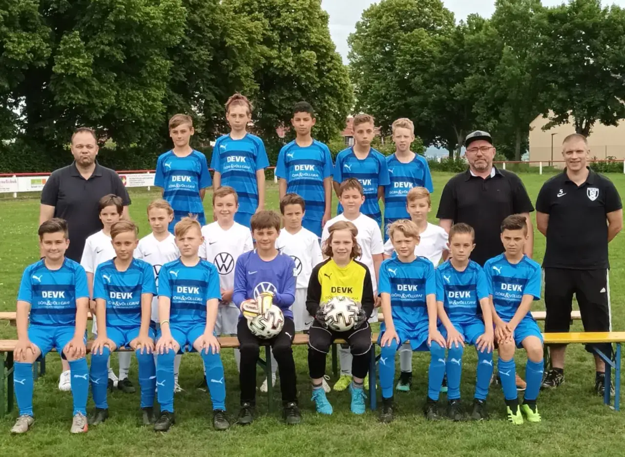 Fu&szlig;ballteam in blauen Trikots, bereit f&uuml;r ein Spiel. Die jugend alter Spieler posieren stolz mit ihren Trainern.