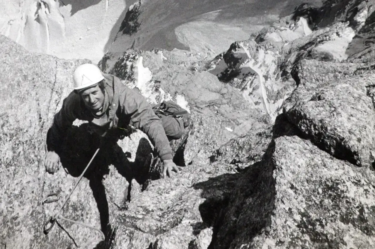 Serge Gousseault, casque blanc, escalade une paroi rocheuse escarpée, le regard déterminé.