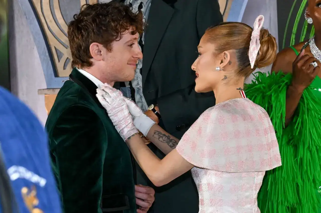 Ariana Grande w białej rękawiczce poprawia kołnierzyk swojego partnera, Ethana Slatera, podczas wydarzenia.