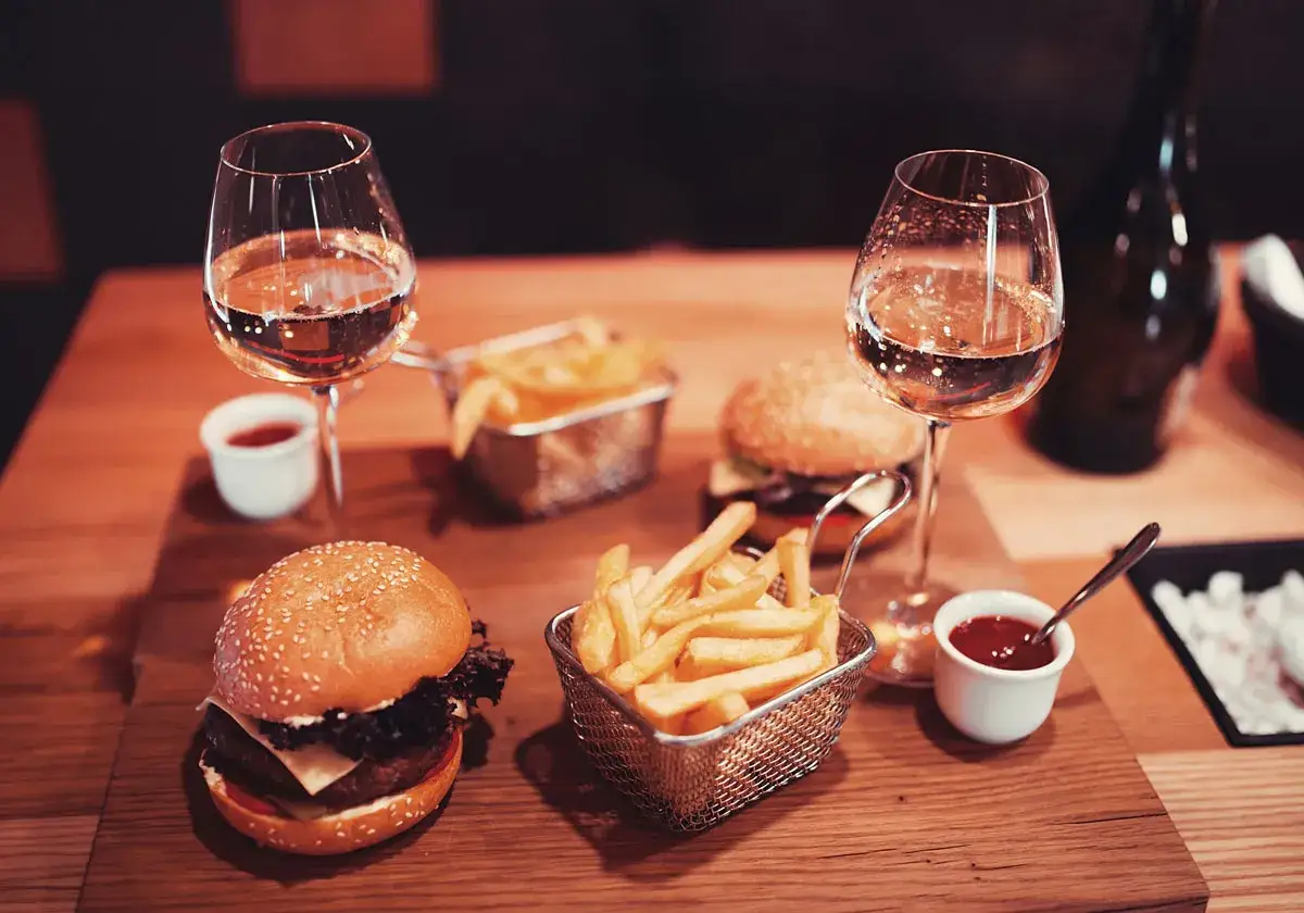 Två glas vin till hamburgare och pommes frites på ett träbord. En perfekt middag för två.
