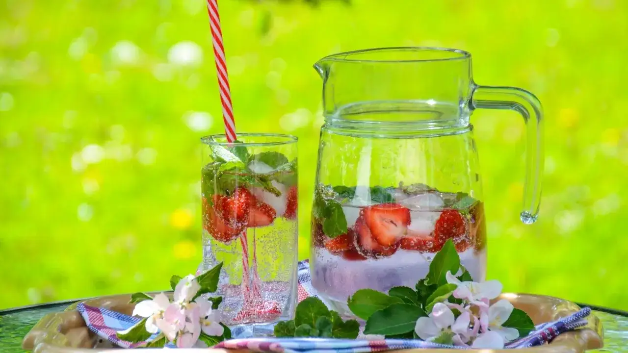 Rinfrescante acqua aromatizzata con fragole e menta, servita in un bicchiere e una caraffa, su un vassoio con fiori.