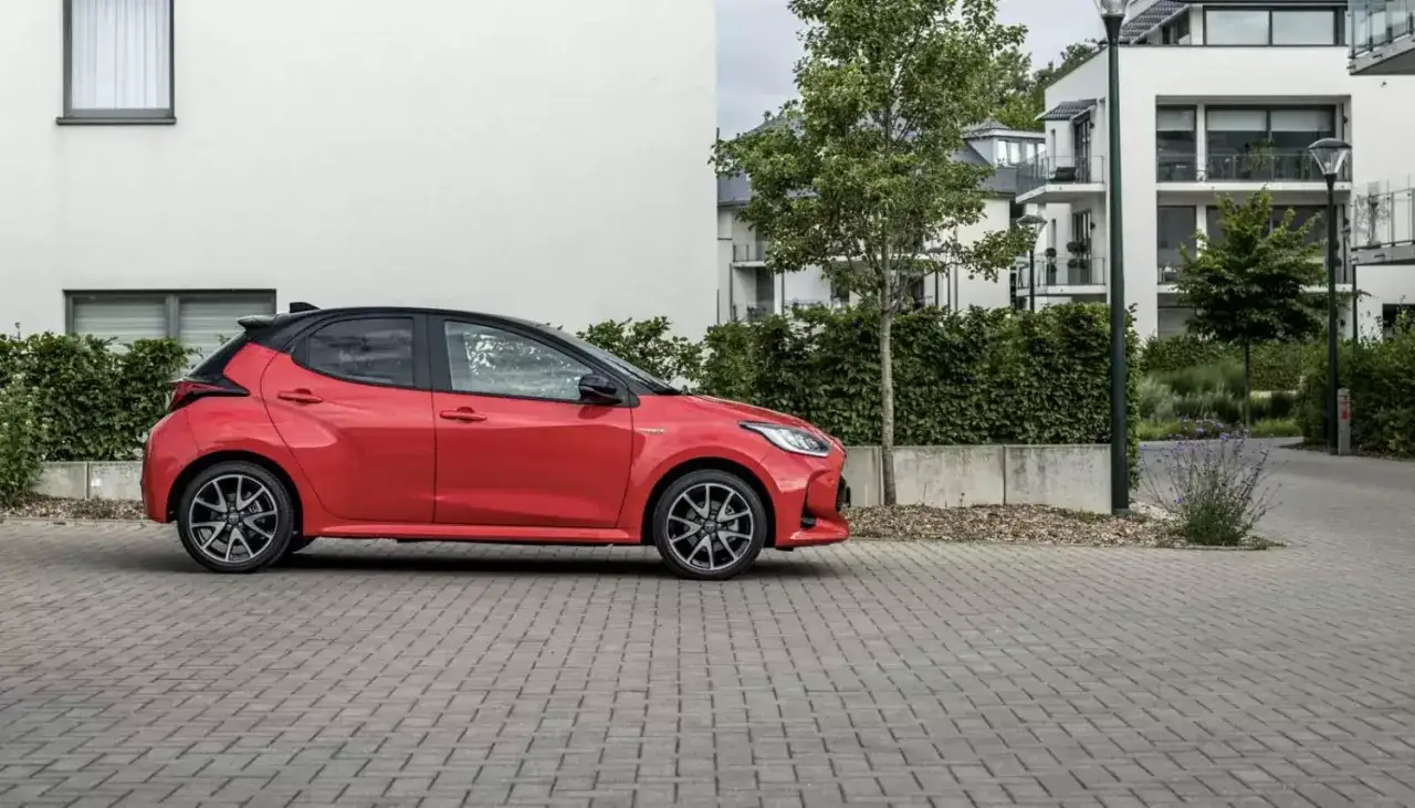 Czerwony, sportowy samochód, idealne pierwsze auto dla dziewczyny, zaparkowany przed nowoczesnym budynkiem.