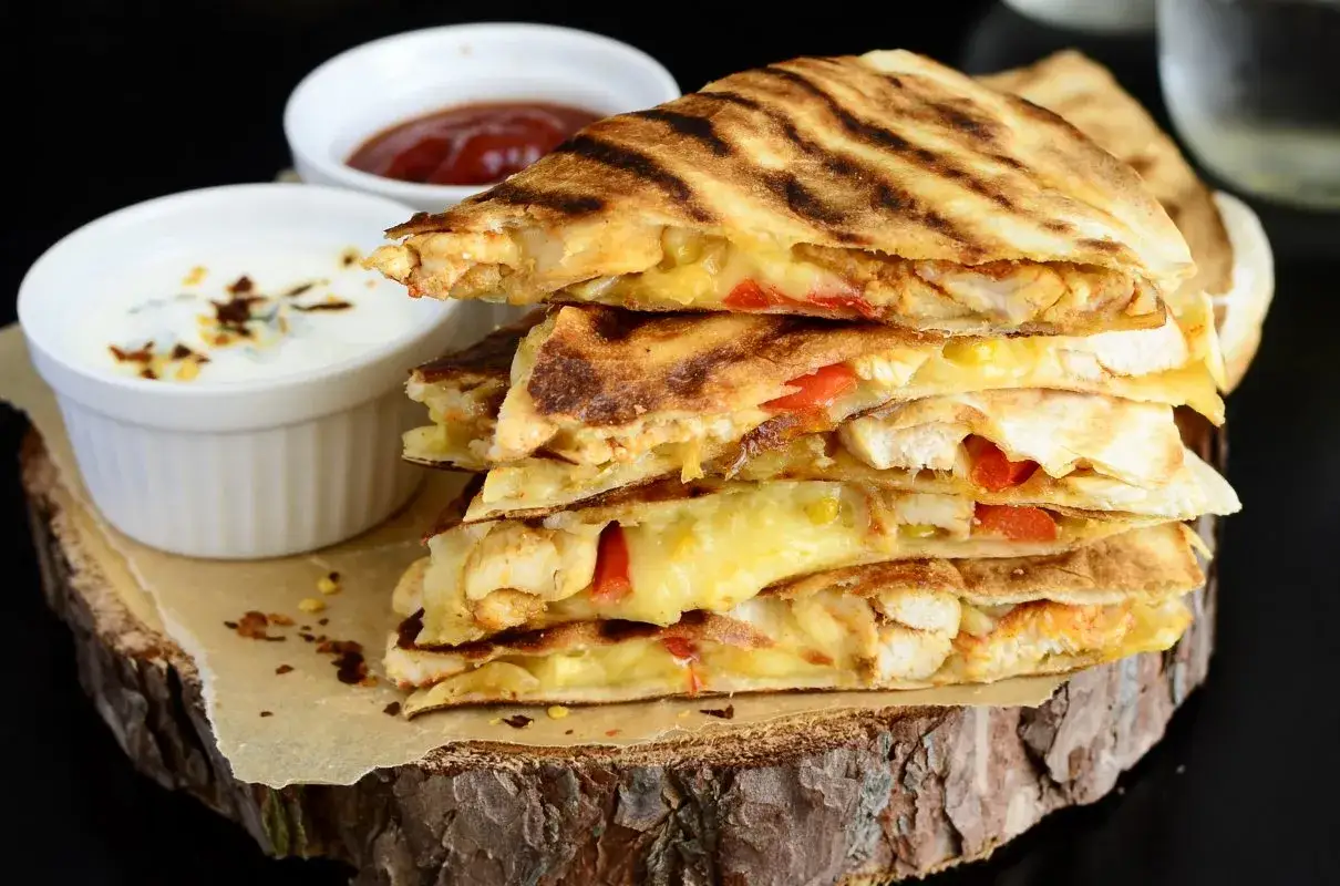 Chrupiąca quesadilla z kurczakiem, roztopionym serem i warzywami, podana z dipem i sosem. Idealna przekąska!